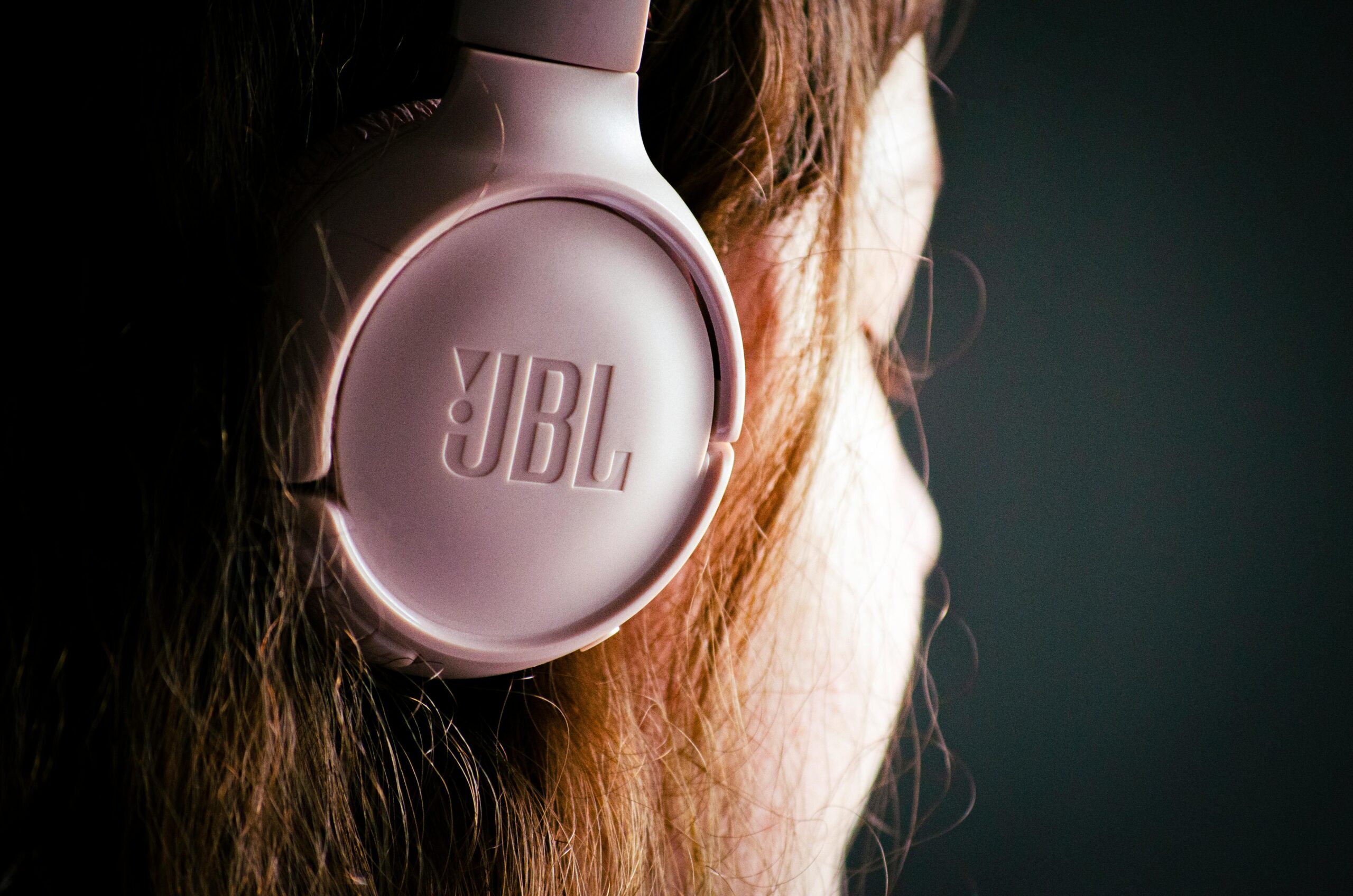 A close-up of a woman wearing pink JBL headphones, showcasing modern audio technology.